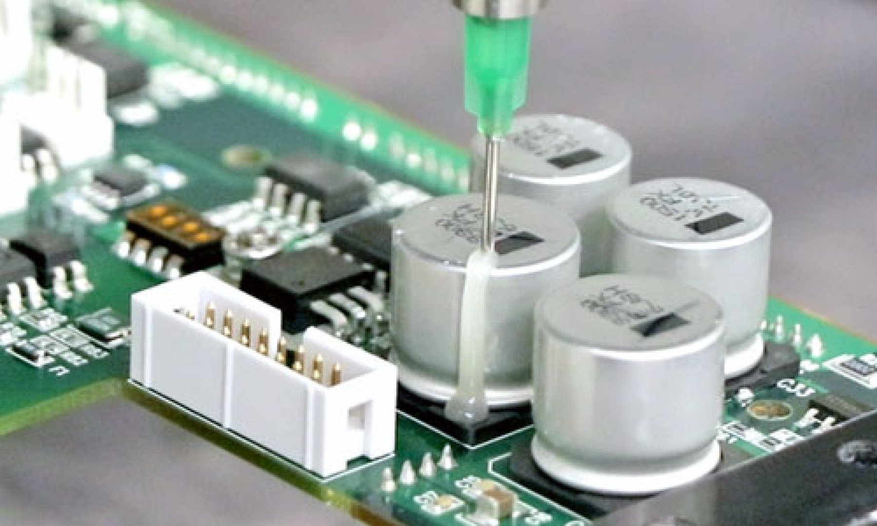 Dymax 9773 low outgassing adhesive is dispensed onto a printed circuit board to ruggedize the electronic components.